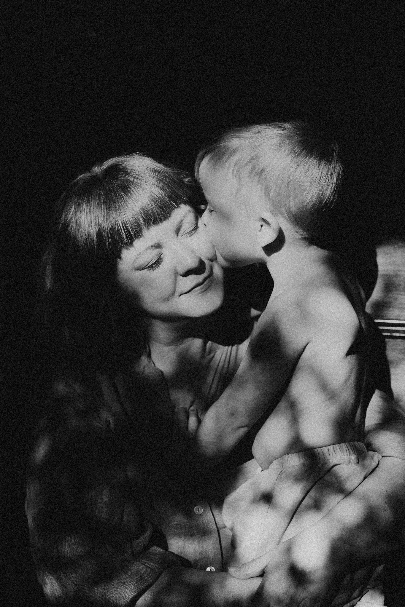 An example of family photography. Black and white photo of child kissing a mother on the cheek.